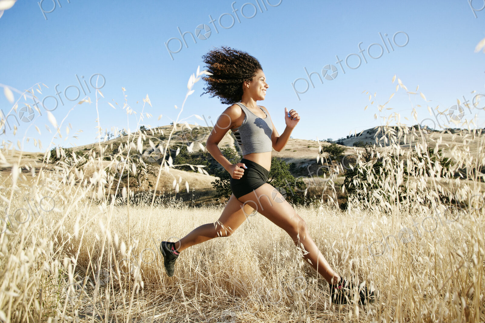Young woman with curly brown hair running in urban park.