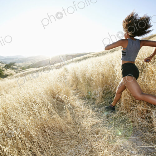 Young woman with curly brown hair running in urban park.