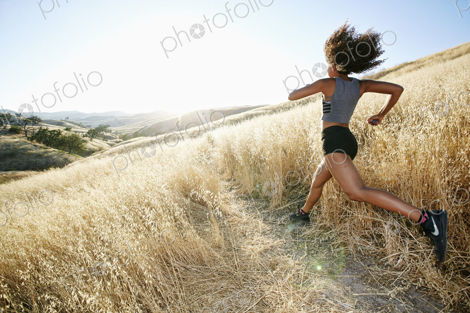 Young woman with curly brown hair running in urban park.