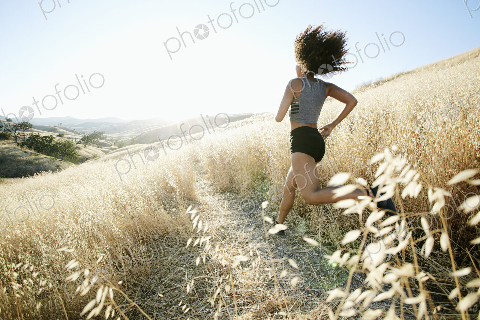 Young woman with curly brown hair running in urban park.