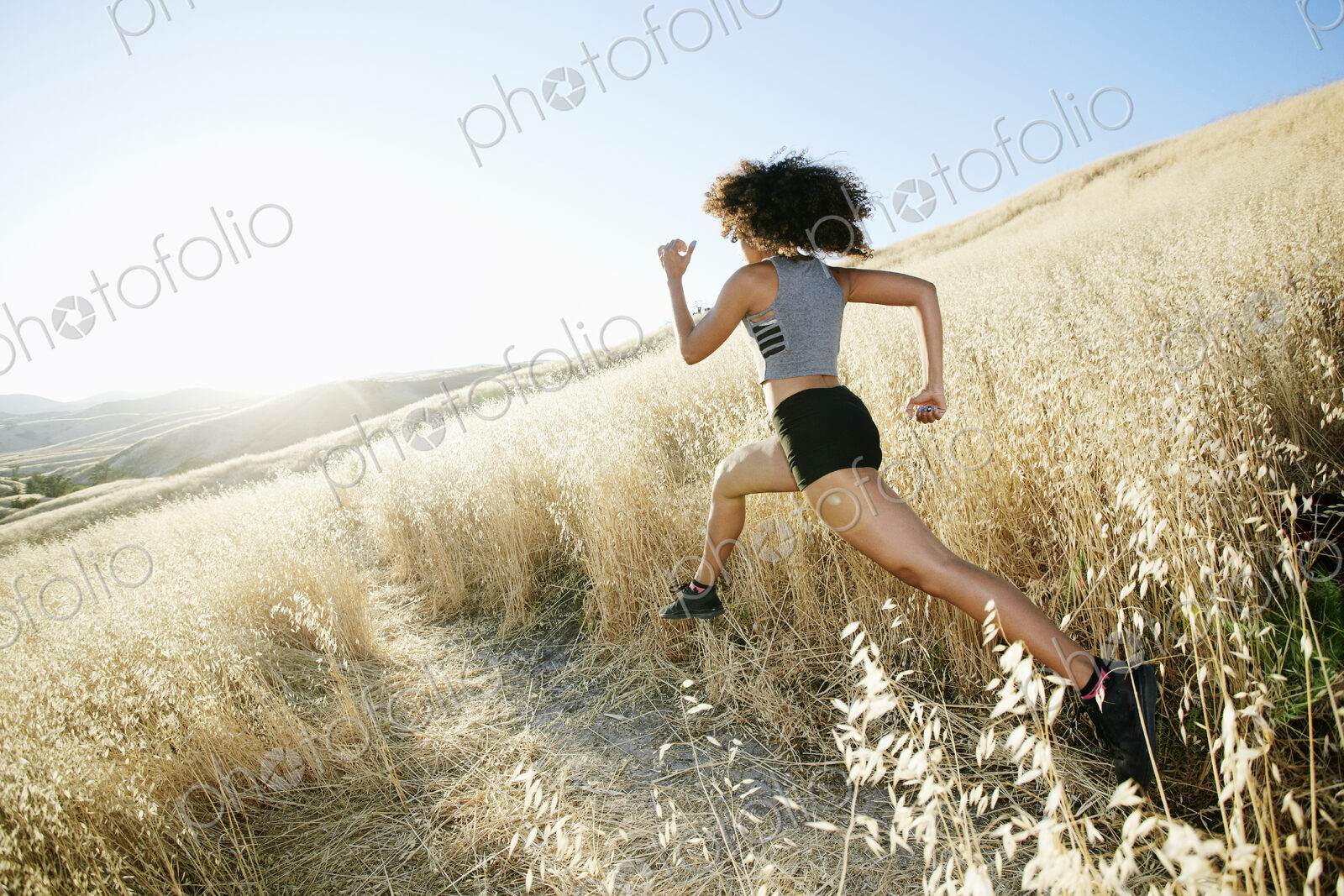 Young woman with curly brown hair running in urban park.