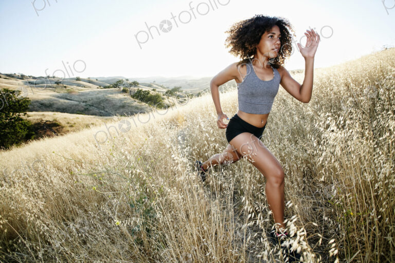 Young woman with curly brown hair running in urban park.