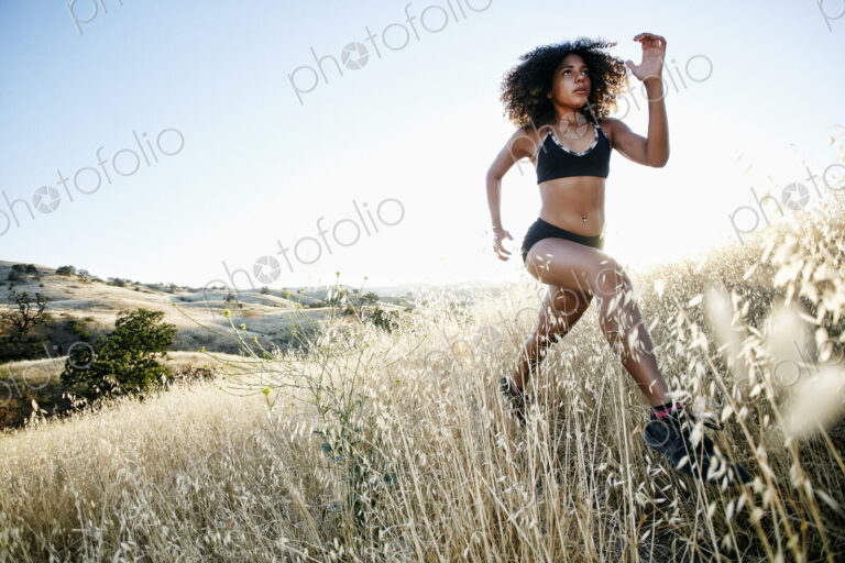 Young woman with curly brown hair running in urban park.