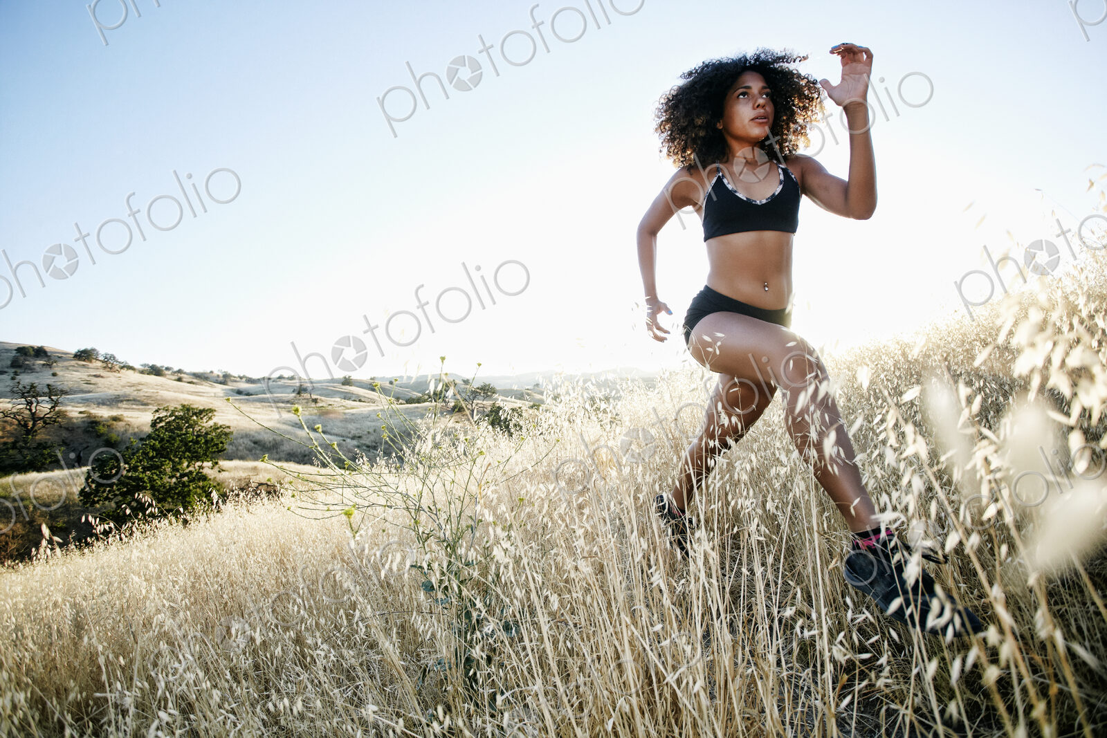 Young woman with curly brown hair running in urban park.
