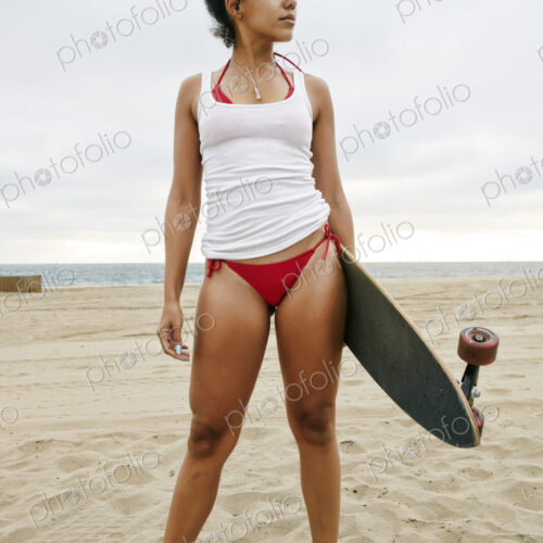 Young woman with curly brown hair wearing white vest and red bikini standing on sandy… Young woman with curly brown hair wearing white vest and red bikini standing on sandy…