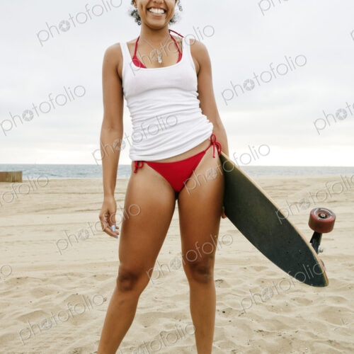 Young woman with curly brown hair wearing white vest and red bikini standing on sandy… Young woman with curly brown hair wearing white vest and red bikini standing on sandy…
