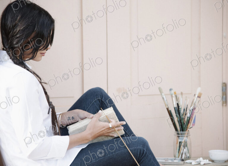 Young woman with long brown hair, holding a sketch book and paint brush.