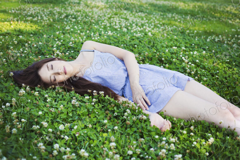 Young woman with long brown hair lying on a lawn.