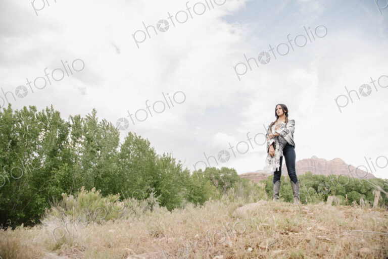 Young woman with long brown hair standing in a prairie under a cloudy sky.