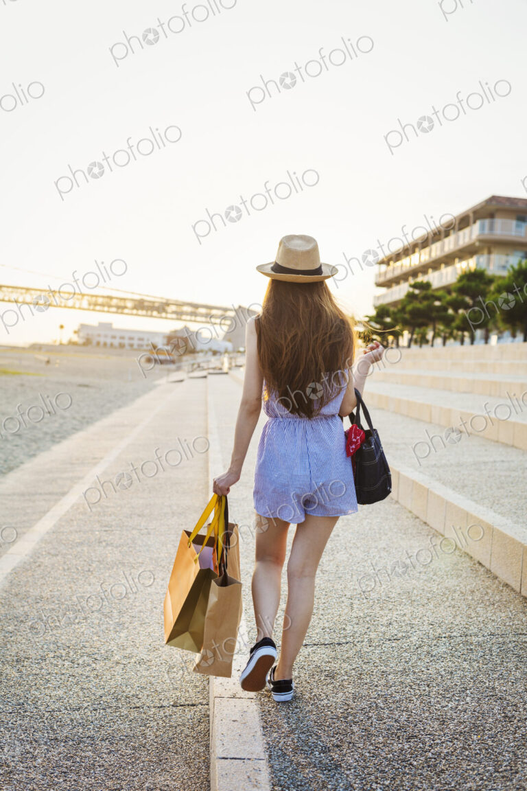 Young woman with long brown hair, wearing Panama hat and carrying shopping bags.