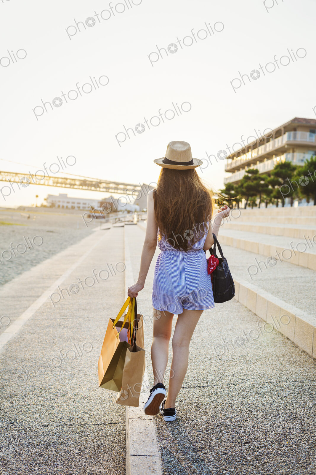 Young woman with long brown hair, wearing Panama hat and carrying shopping bags.