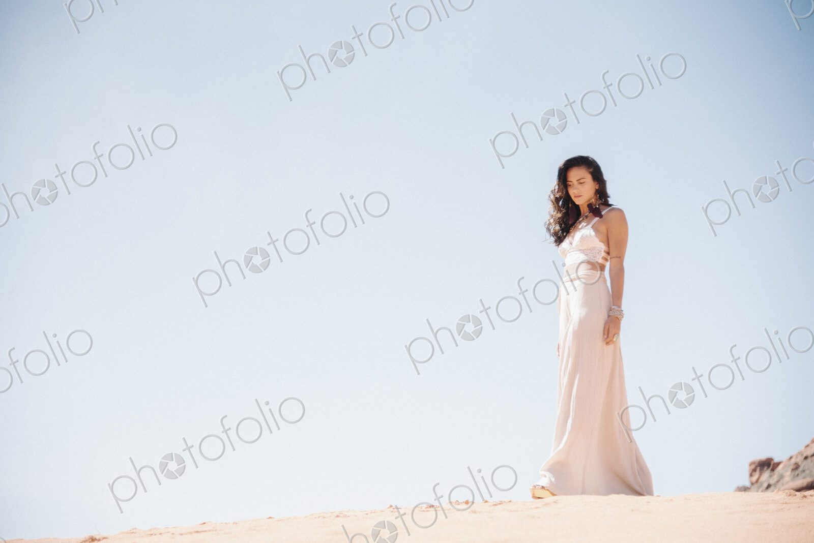 Young woman with long brown hair, wearing a long white dress, standing in a desert.