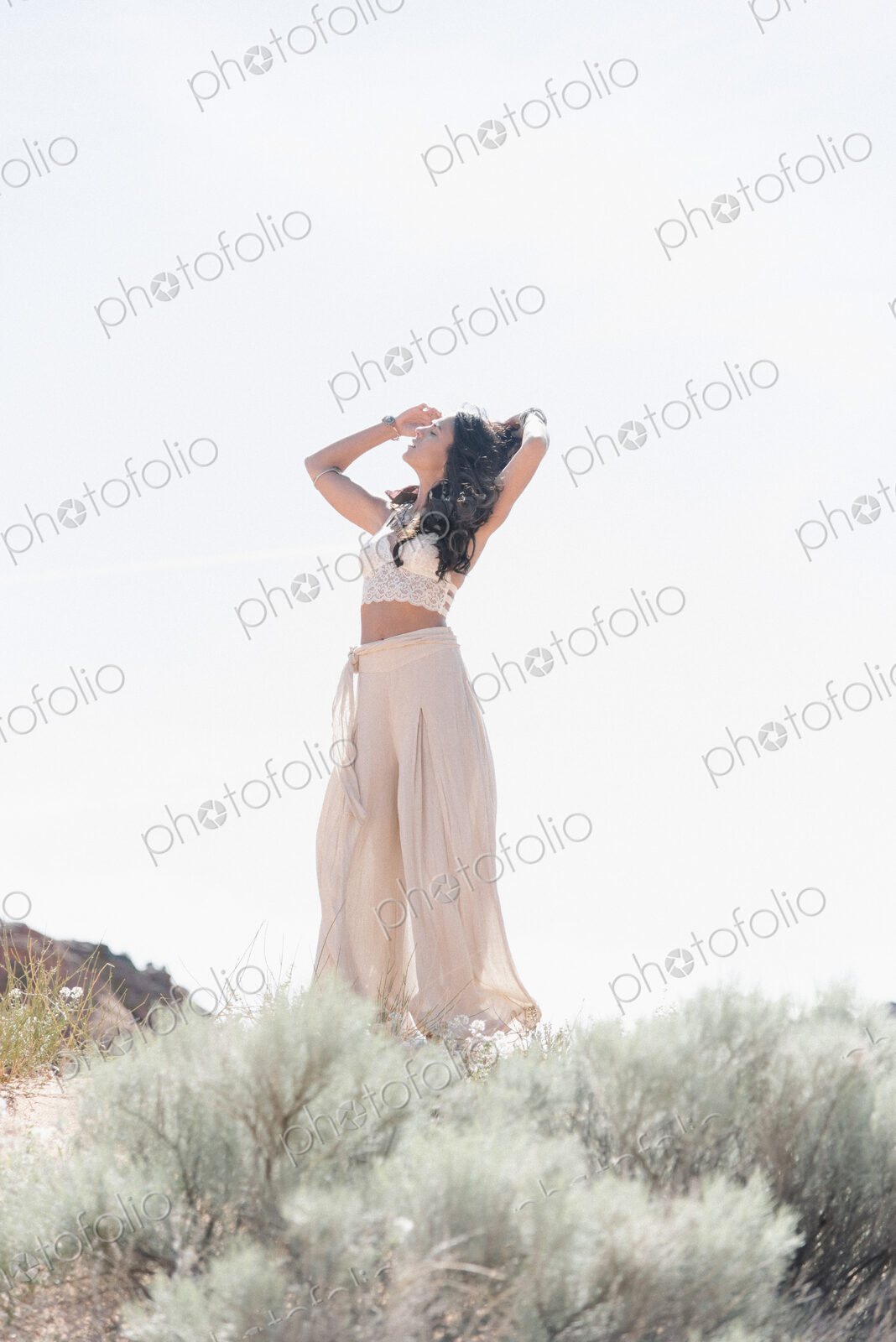 Young woman with long brown hair, wearing a long white dress, standing in the prairie.