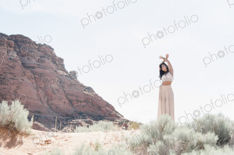Young woman with long brown hair, wearing a long white dress, standing in the prairie.