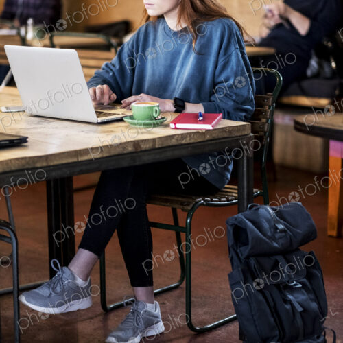 Young woman with long red hair sitting at table, working on laptop computer. Young woman with long red hair sitting at table, working on laptop computer.