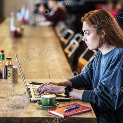 Young woman with long red hair sitting at table, working on laptop computer. Young woman with long red hair sitting at table, working on laptop computer.