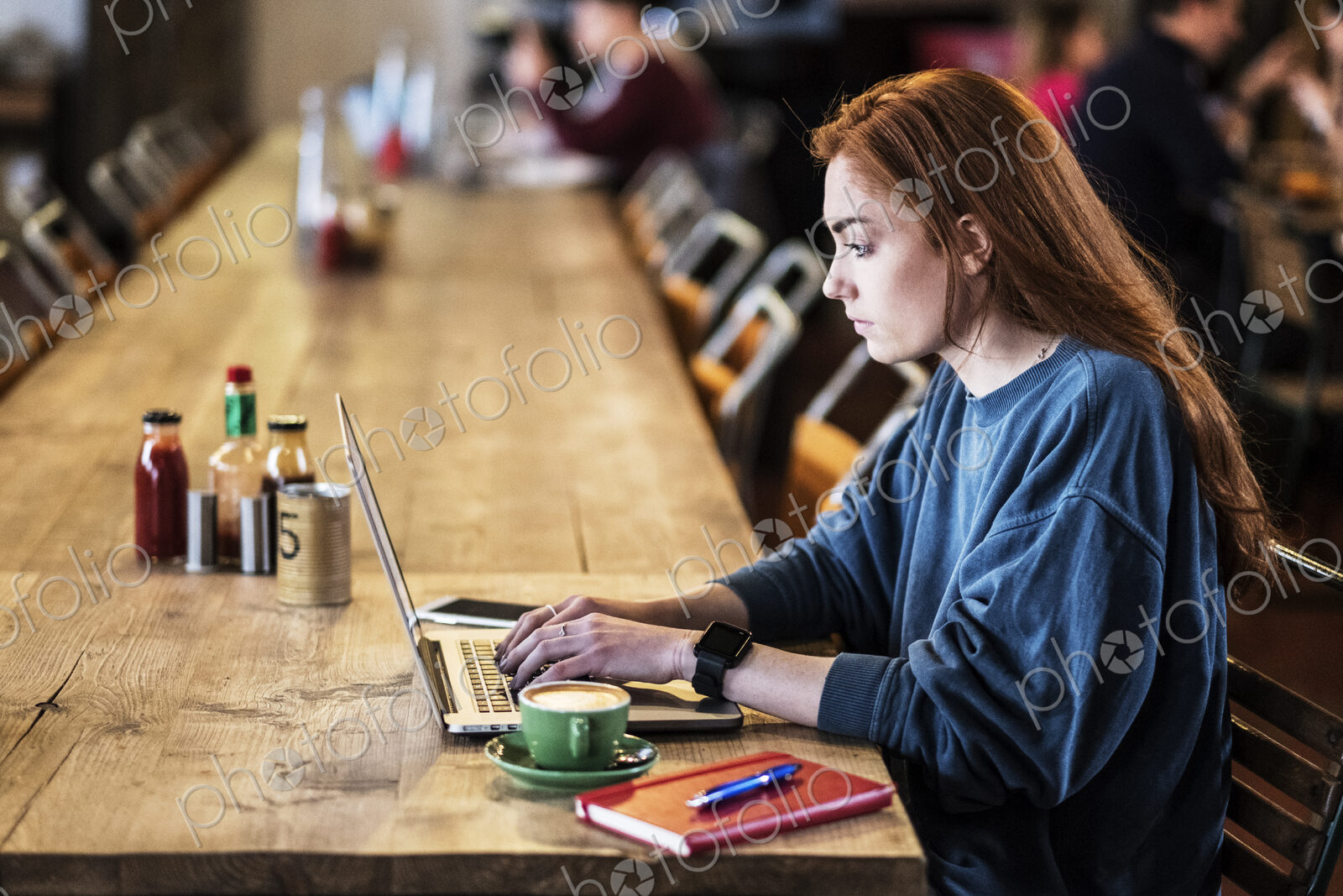 Young woman with long red hair sitting at table, working on laptop computer.