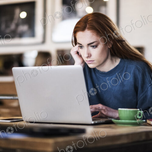 Young woman with long red hair sitting at table, working on laptop computer. Young woman with long red hair sitting at table, working on laptop computer.