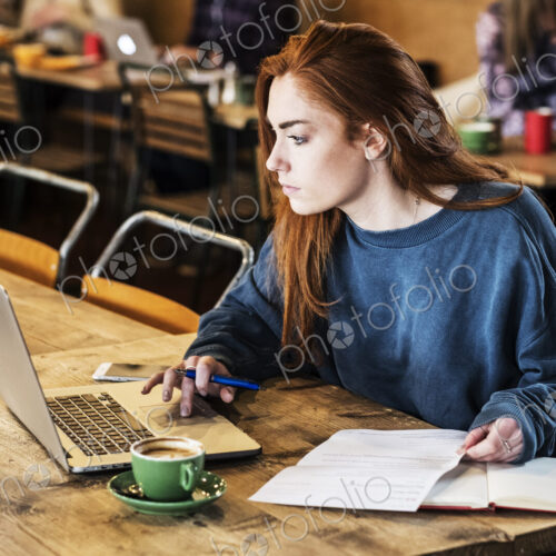 Young woman with long red hair sitting at table, working on laptop computer. Young woman with long red hair sitting at table, working on laptop computer.