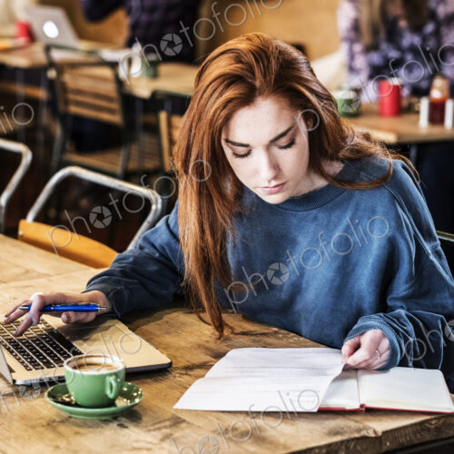 Young woman with long red hair sitting at table, working on laptop computer. Young woman with long red hair sitting at table, working on laptop computer.