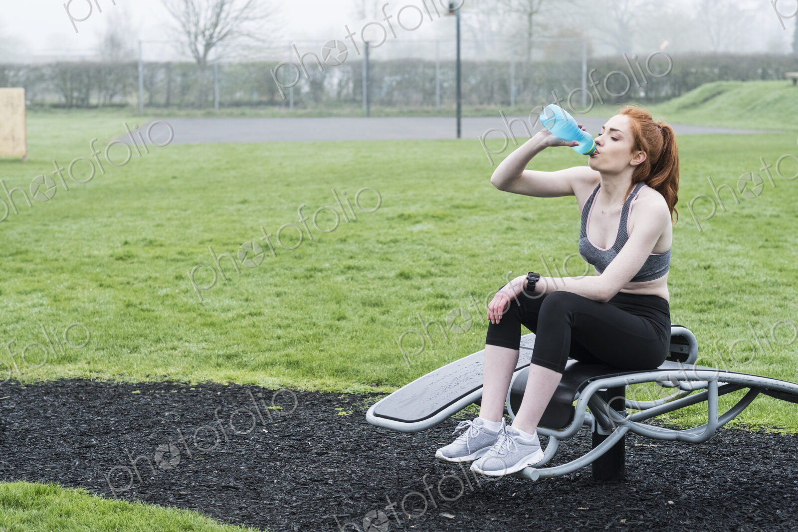 Young woman with long red hair wearing sportswear, exercising outdoors.
