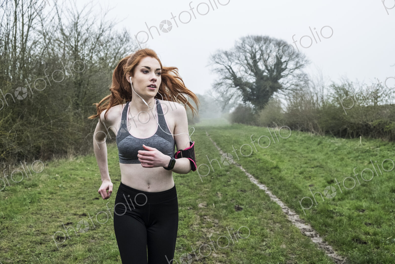 Young woman with long red hair wearing sportswear, exercising outdoors.