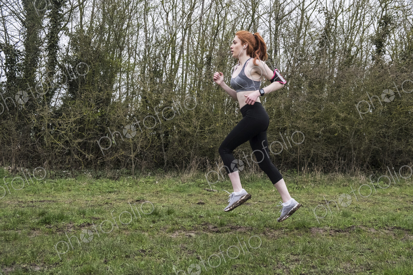 Young woman with long red hair wearing sportswear, exercising outdoors.