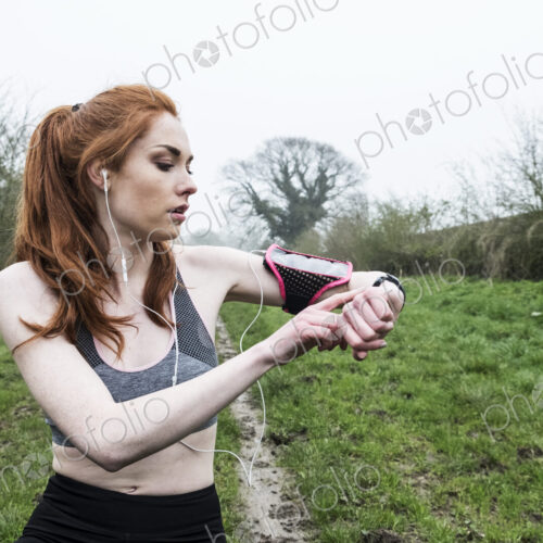 Young woman with long red hair wearing sportswear, exercising outdoors, checking her… Young woman with long red hair wearing sportswear, exercising outdoors, checking her…