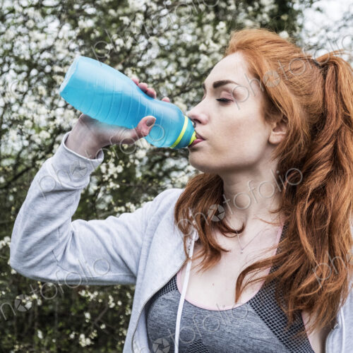 Young woman with long red hair wearing sportswear, exercising outdoors, drinking from… Young woman with long red hair wearing sportswear, exercising outdoors, drinking from…