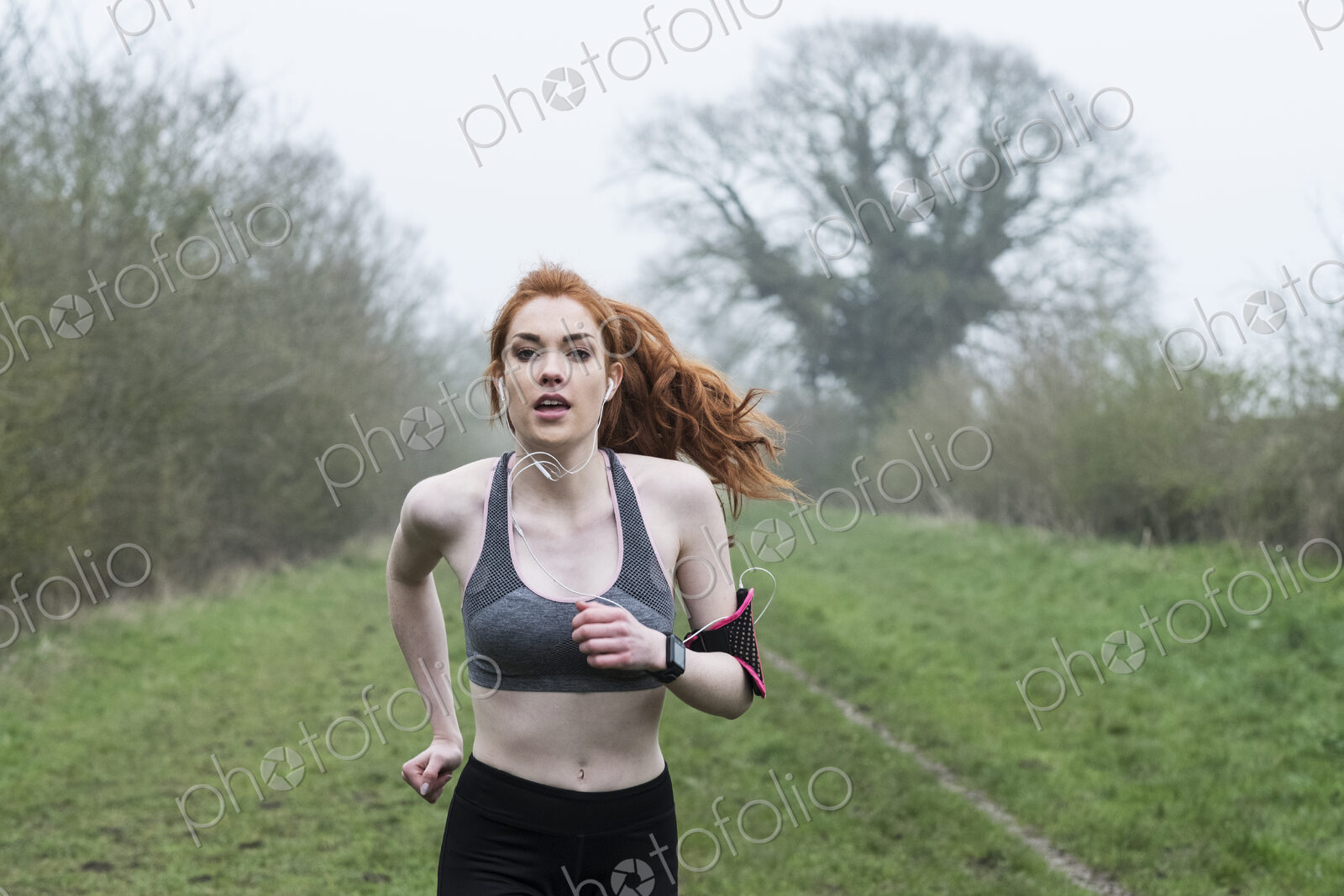 Young woman with long red hair wearing sportswear, exercising outdoors, looking at camera.