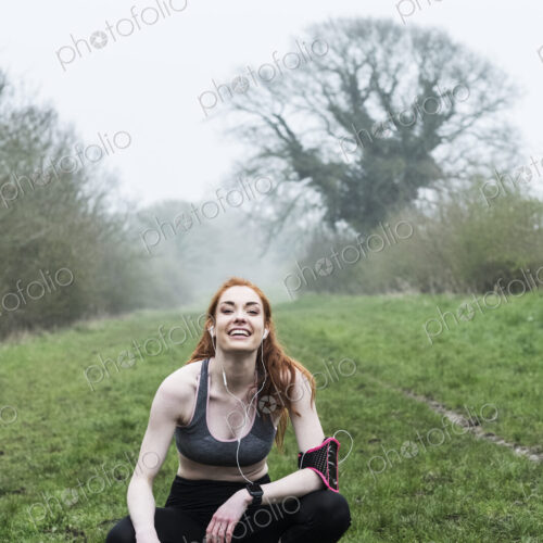 Young woman with long red hair wearing sportswear, exercising outdoors, looking at camera. Young woman with long red hair wearing sportswear, exercising outdoors, looking at camera.