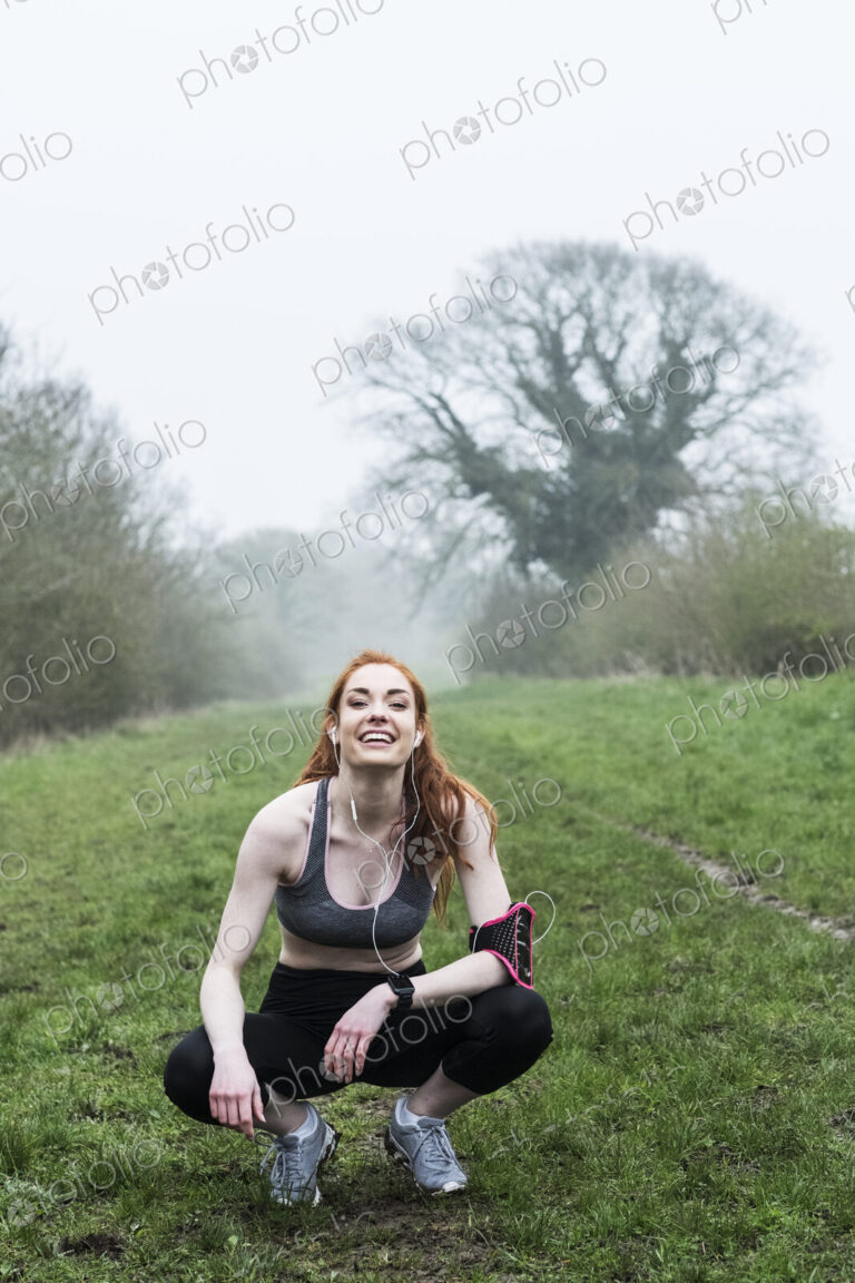 Young woman with long red hair wearing sportswear, exercising outdoors, looking at camera.