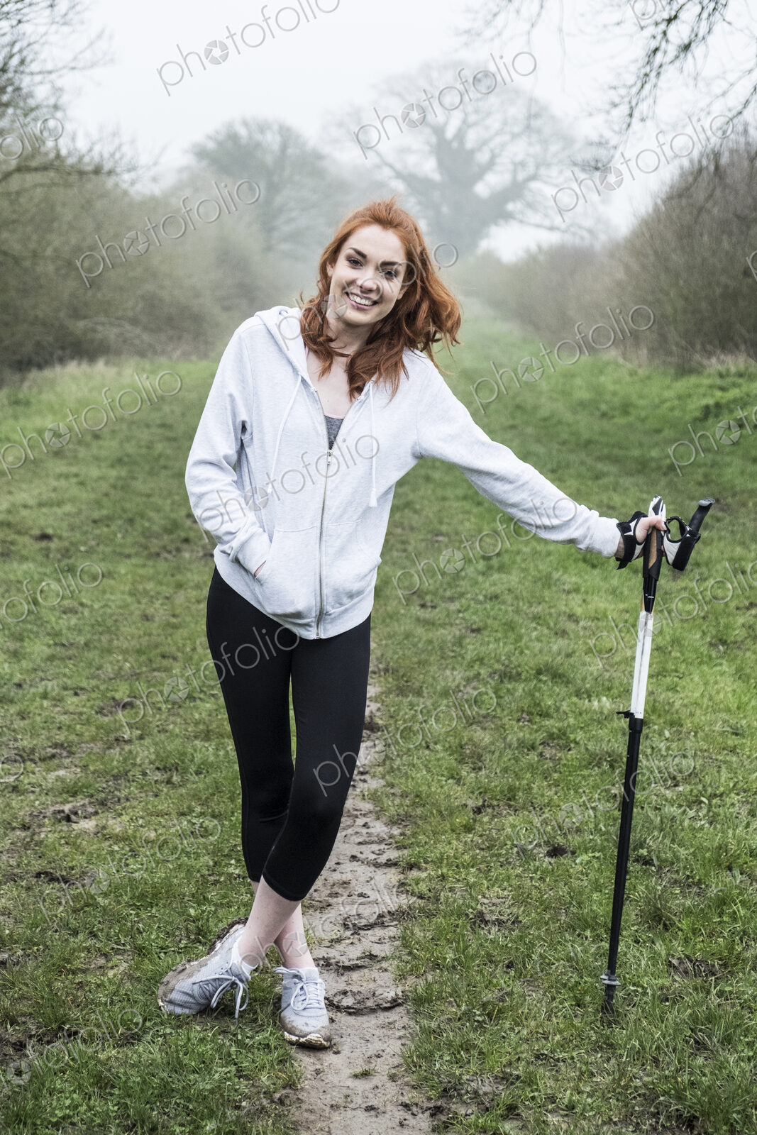 Young woman with long red hair wearing sportswear, exercising outdoors, looking at camera.