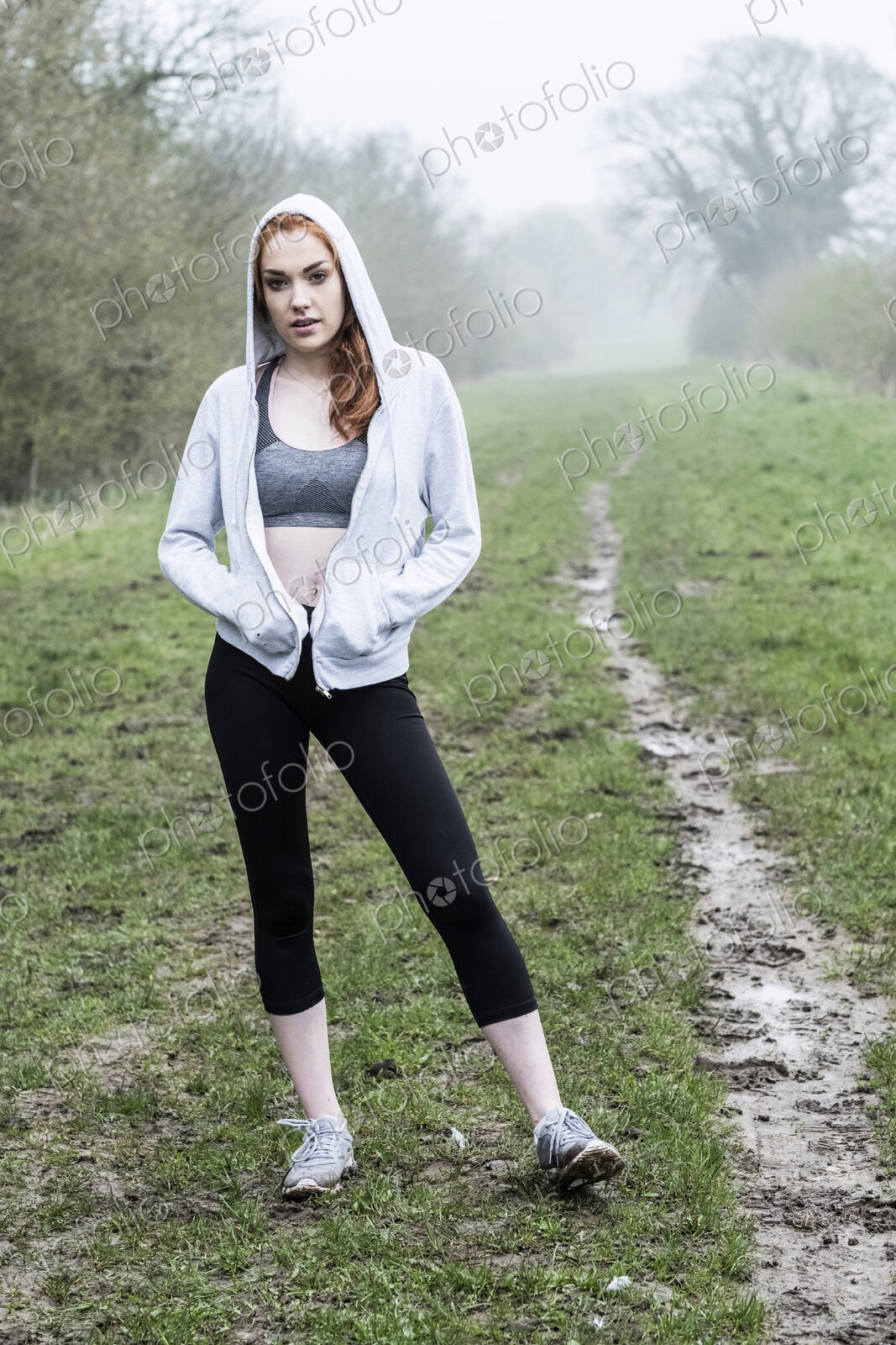 Young woman with long red hair wearing sportswear, exercising outdoors, looking at camera.