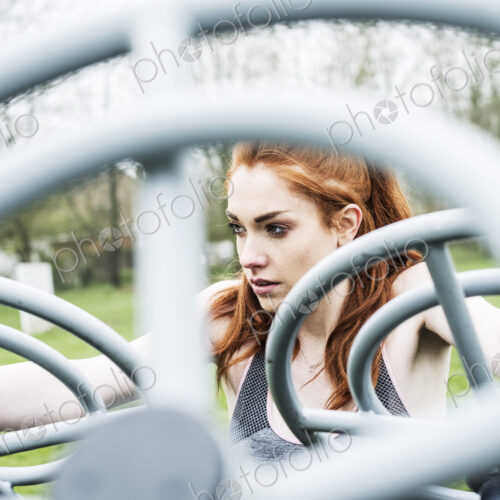 Young woman with long red hair wearing sportswear, using outdoor exercise machine. Young woman with long red hair wearing sportswear, using outdoor exercise machine.