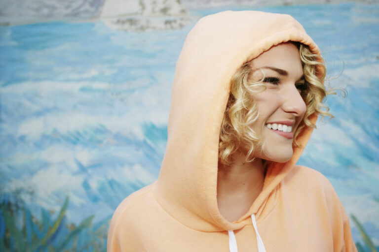 Profile portrait of smiling woman with curly blond hair wearing pink hoodie.