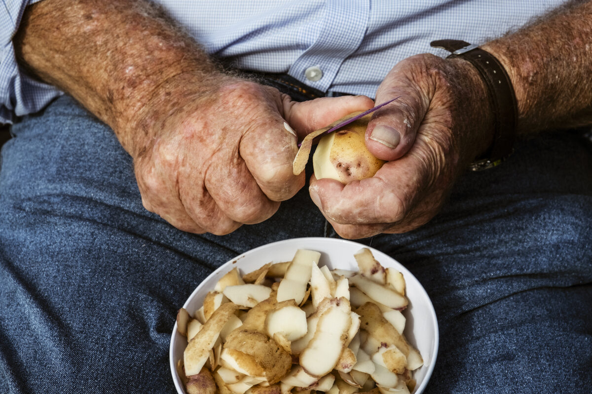 Objects category — A man seated using a sharp knife to peel potatoes. A man seated using a sharp knife to peel potatoes.