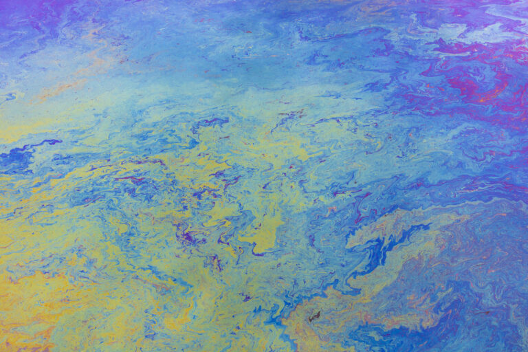 Spilled diesel fuel on surface on ocean water, close up, blue and yellow patterns.